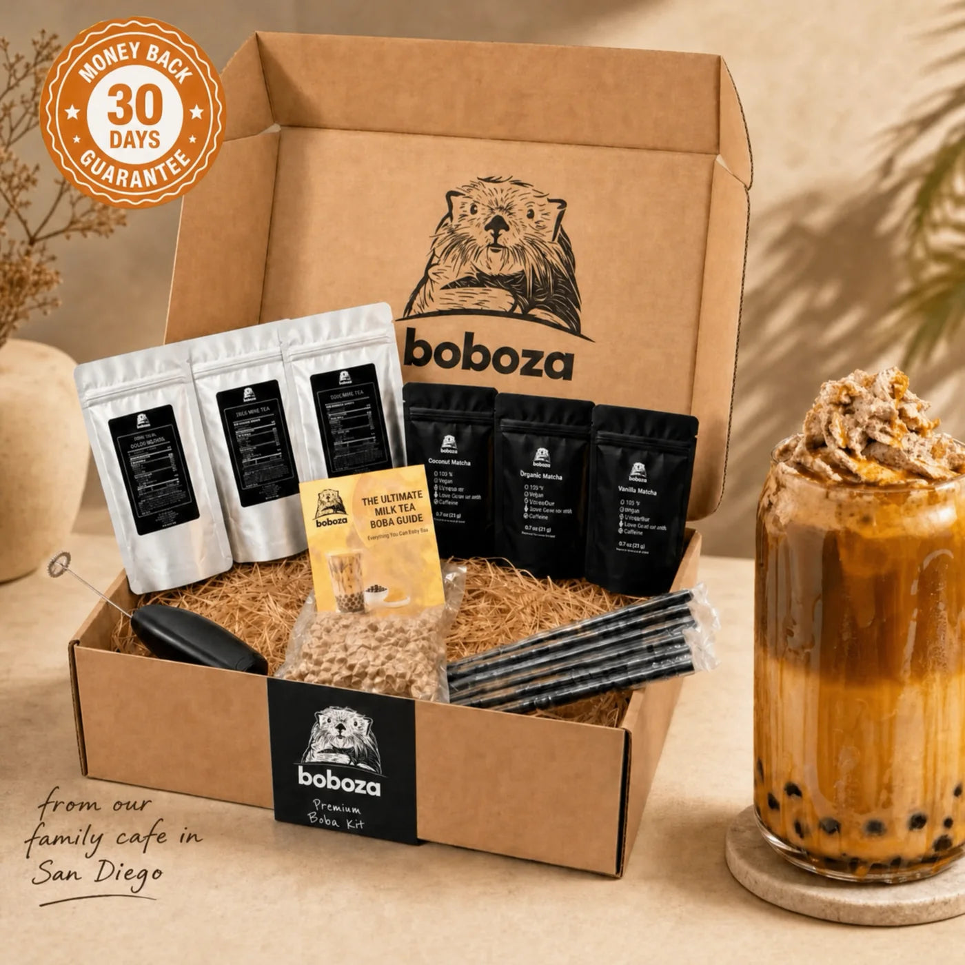 Open Boboza premium boba kit box with flavor pouches, tapioca pearls, straws, mixer and guide, next to a finished iced boba drink