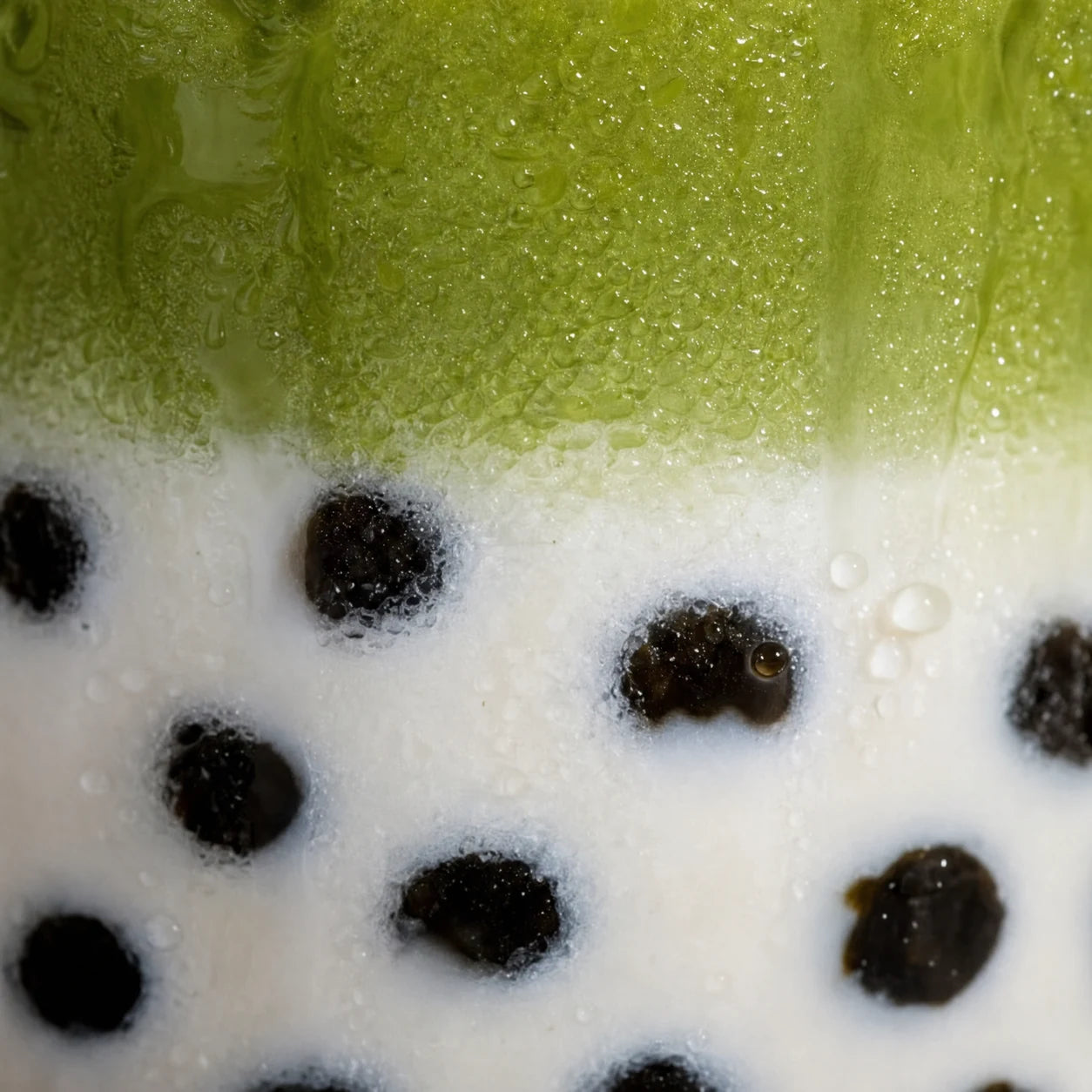 Close-up of an iced matcha latte where dark boba pearls sit suspended in the milk, showing how chewy and glossy they cook up