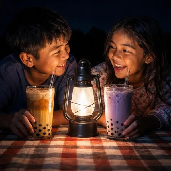 Two kids sharing boba by lantern light on a picnic blanket