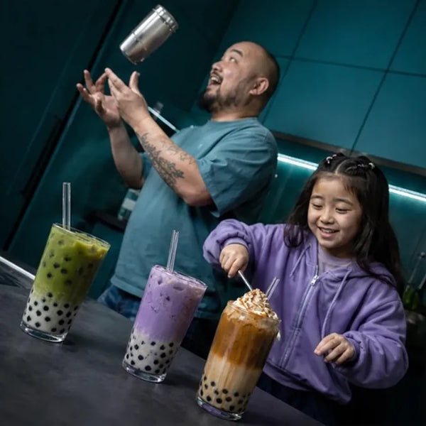Dad flipping a shaker while daughter builds her boba