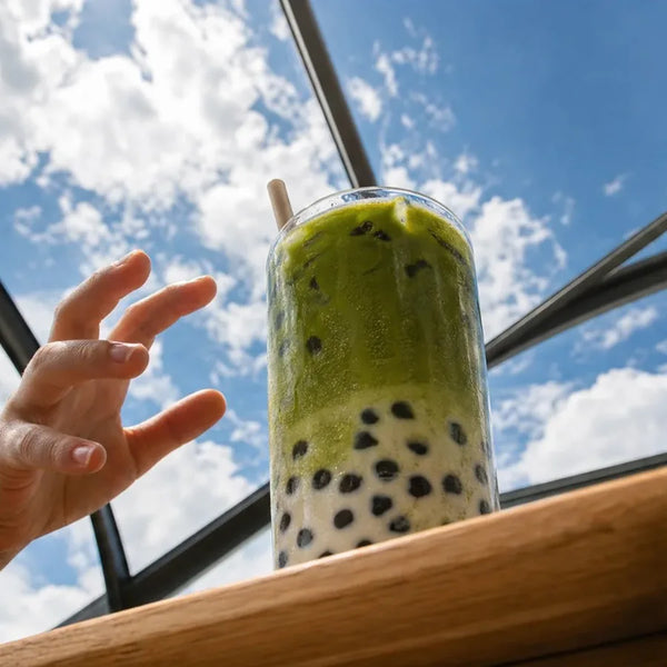 Hand reaching for a matcha boba against the sky