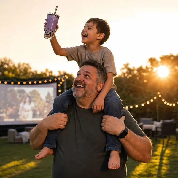 Boy on dads shoulders raising boba at an outdoor movie night