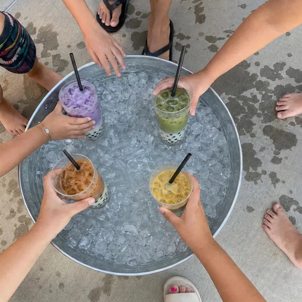 Four boba drinks chilling in an ice bucket, hands reaching in