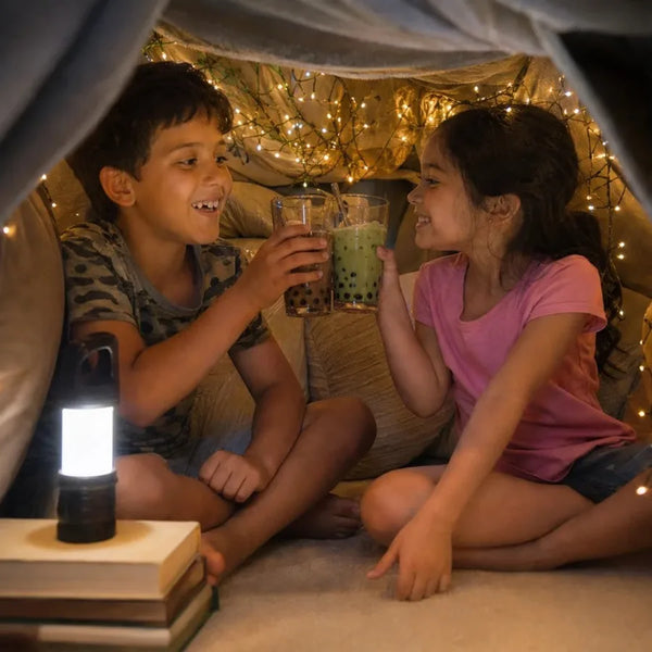 Two kids toasting boba inside a blanket fort with fairy lights