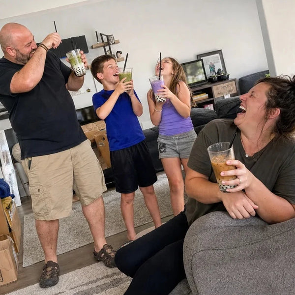 Family of four laughing with boba drinks among moving boxes in the living room