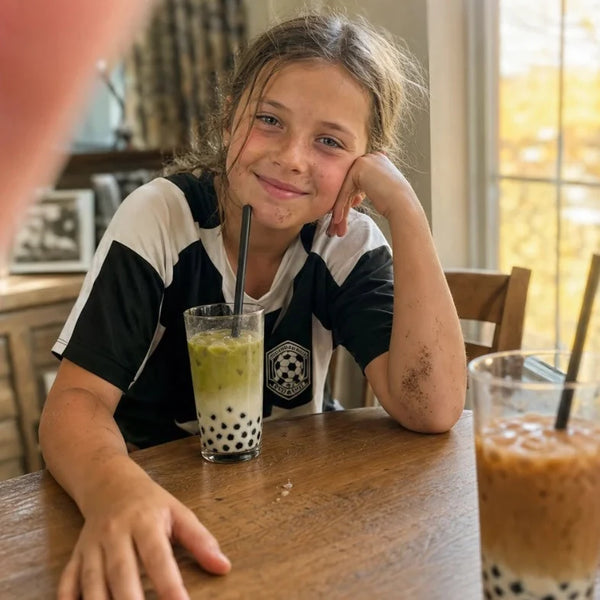 Girl in a soccer jersey smiling at the table with a matcha boba