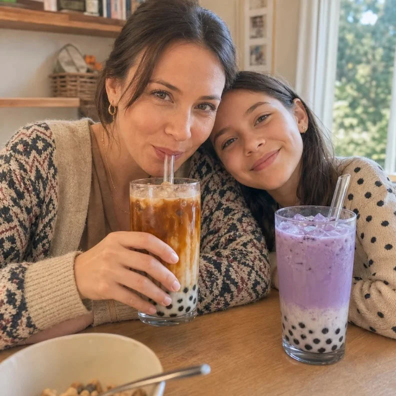 Mom sipping an iced coffee boba while her daughter leans on her shoulder with a taro boba at the kitchen table