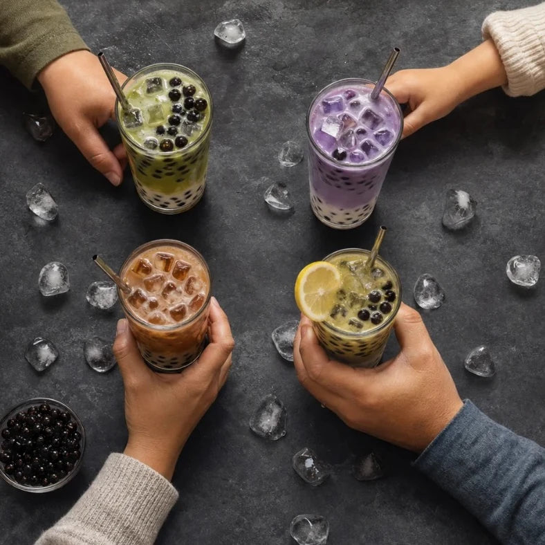 Overhead view of four hands each reaching for a different Boboza drink with boba pearls, matcha, taro, Thai tea and lemon green tea, on a dark stone table scattered with ice